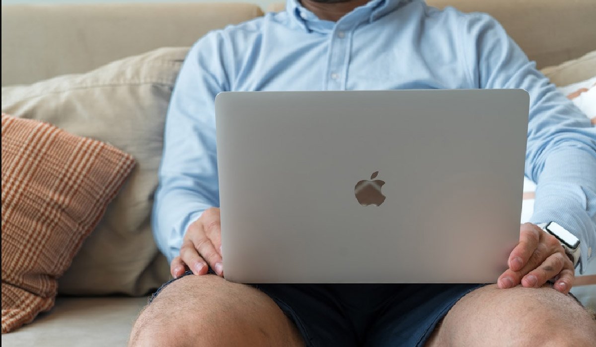 A man on a couch with a laptop, exploring online faxing software tool and its effects on business communication strategies.